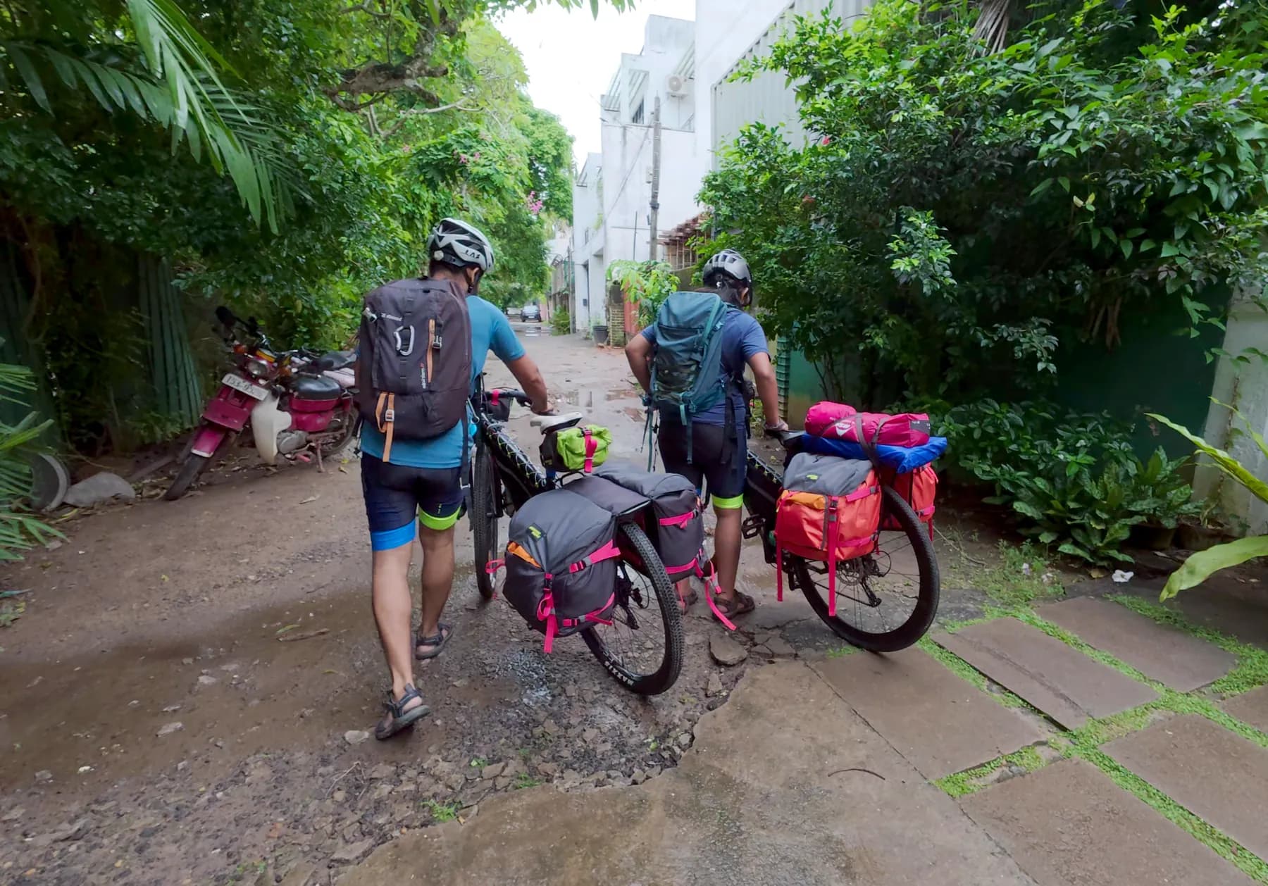 Intiaz and Subah wheel their fully loaded touring bicycles along a wet lane in Colombo