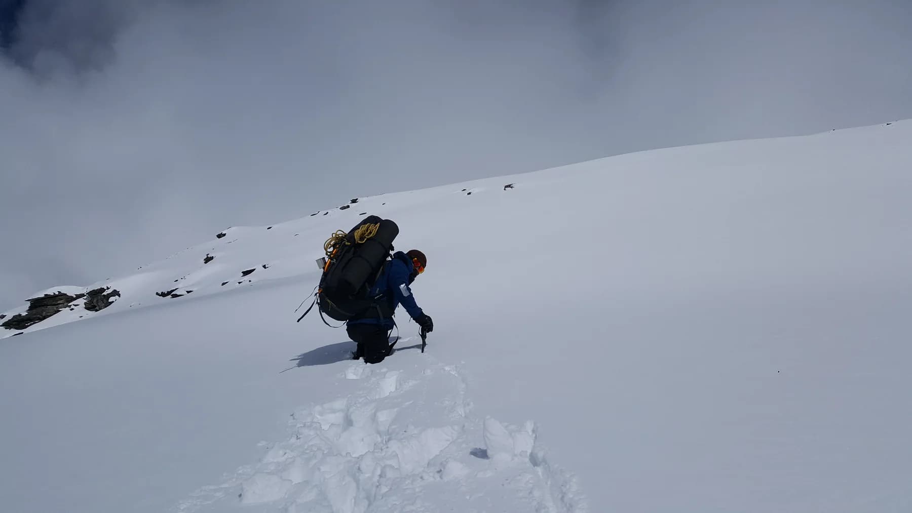 A climber with a loaded backpack and ice axe moving through deep snow